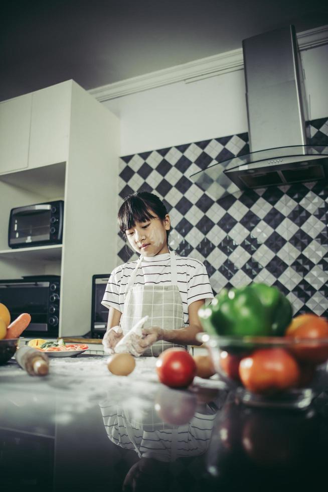 schattig klein meisje kneedt bloemdeeg in de keuken foto