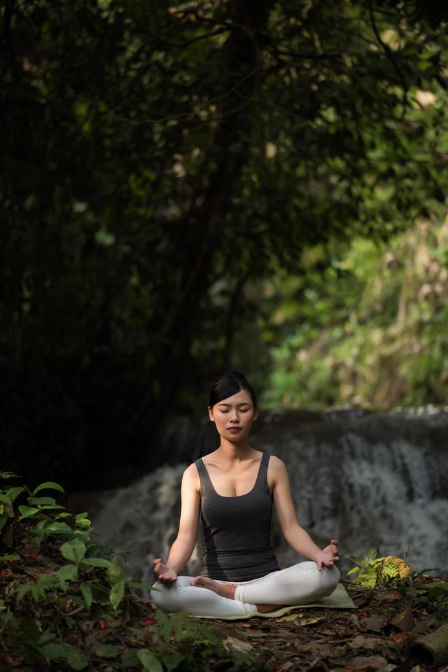 jonge vrouw in een yoga-pose zit in de buurt van een waterval foto
