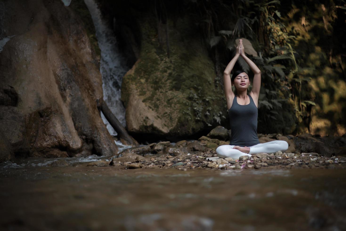 jonge vrouw in een yoga-pose zit in de buurt van een waterval foto