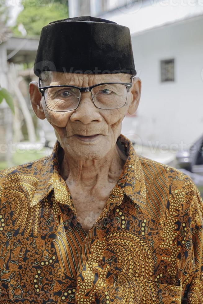 een portret van een oud Aziatisch Mens vervelend batik overhemd en bril foto