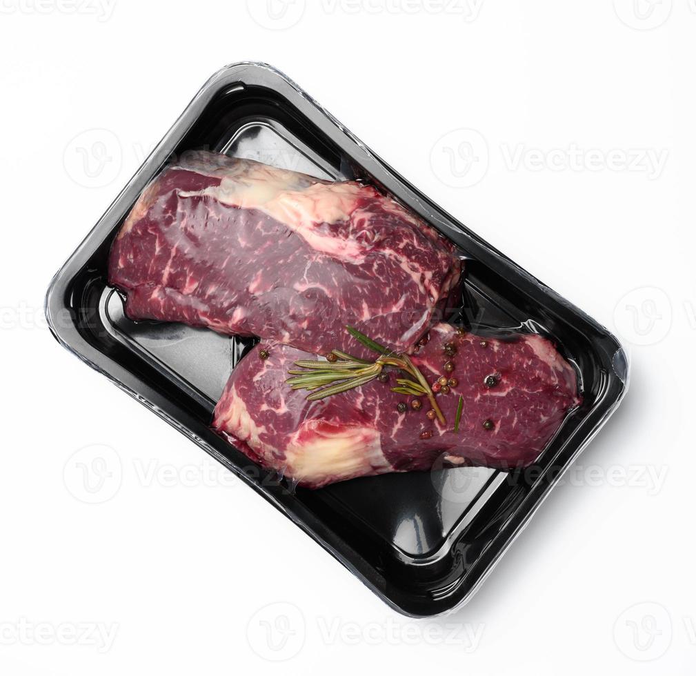 twee rauw rundvlees steaks in een plastic houder met specerijen en gevacumeerd Aan een wit achtergrond, verpakking voor langetermijn opslagruimte foto