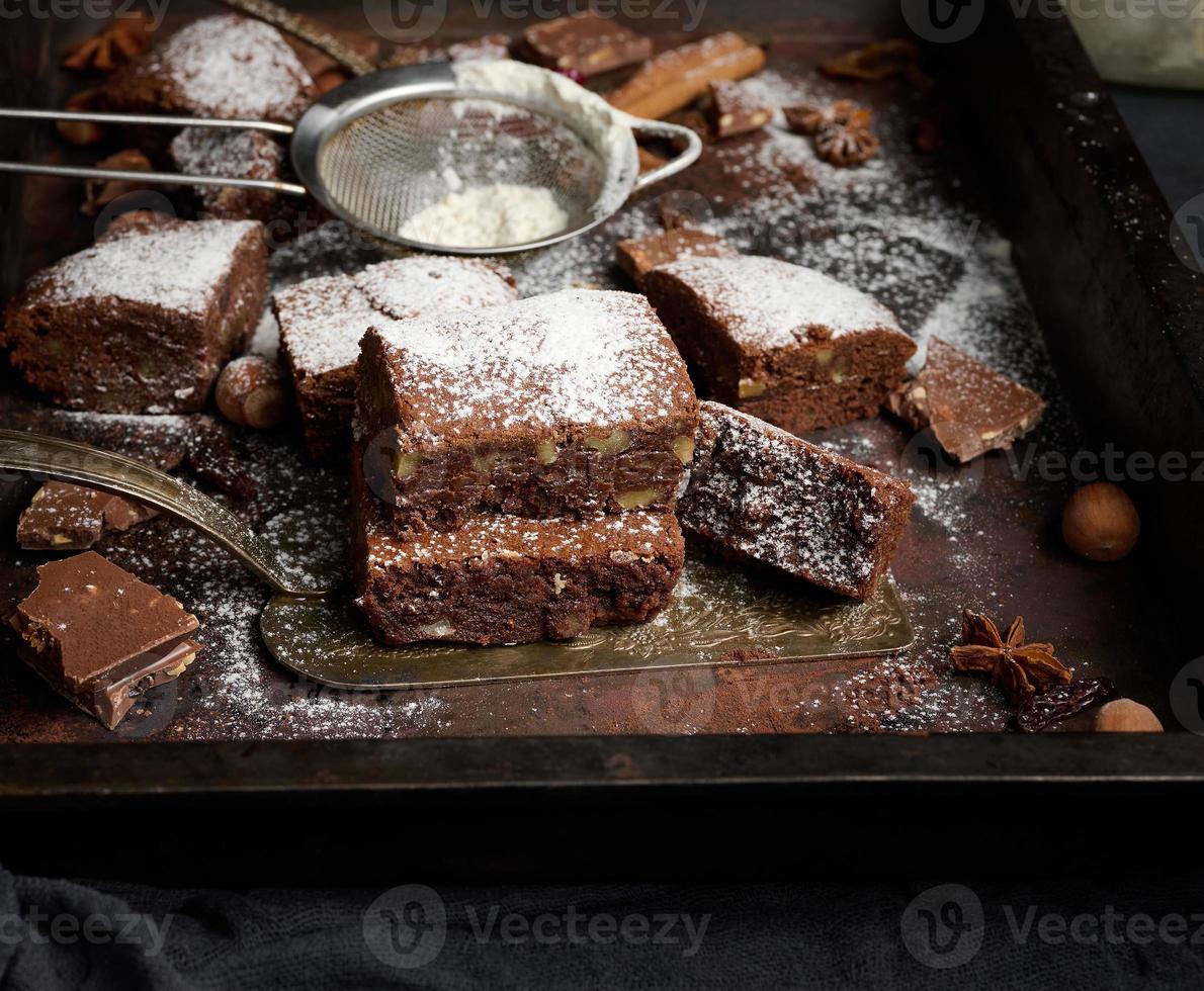 gebakken plein stukken van chocola brownie besprenkeld met gepoederd suiker Aan de tafel foto