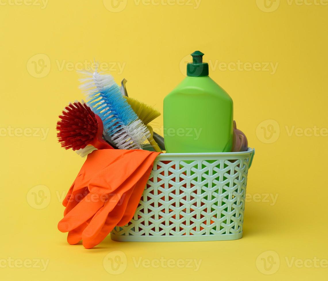 blauw plastic mand met borstels, sponzen en rubber handschoenen voor schoonmaak, geel achtergrond foto