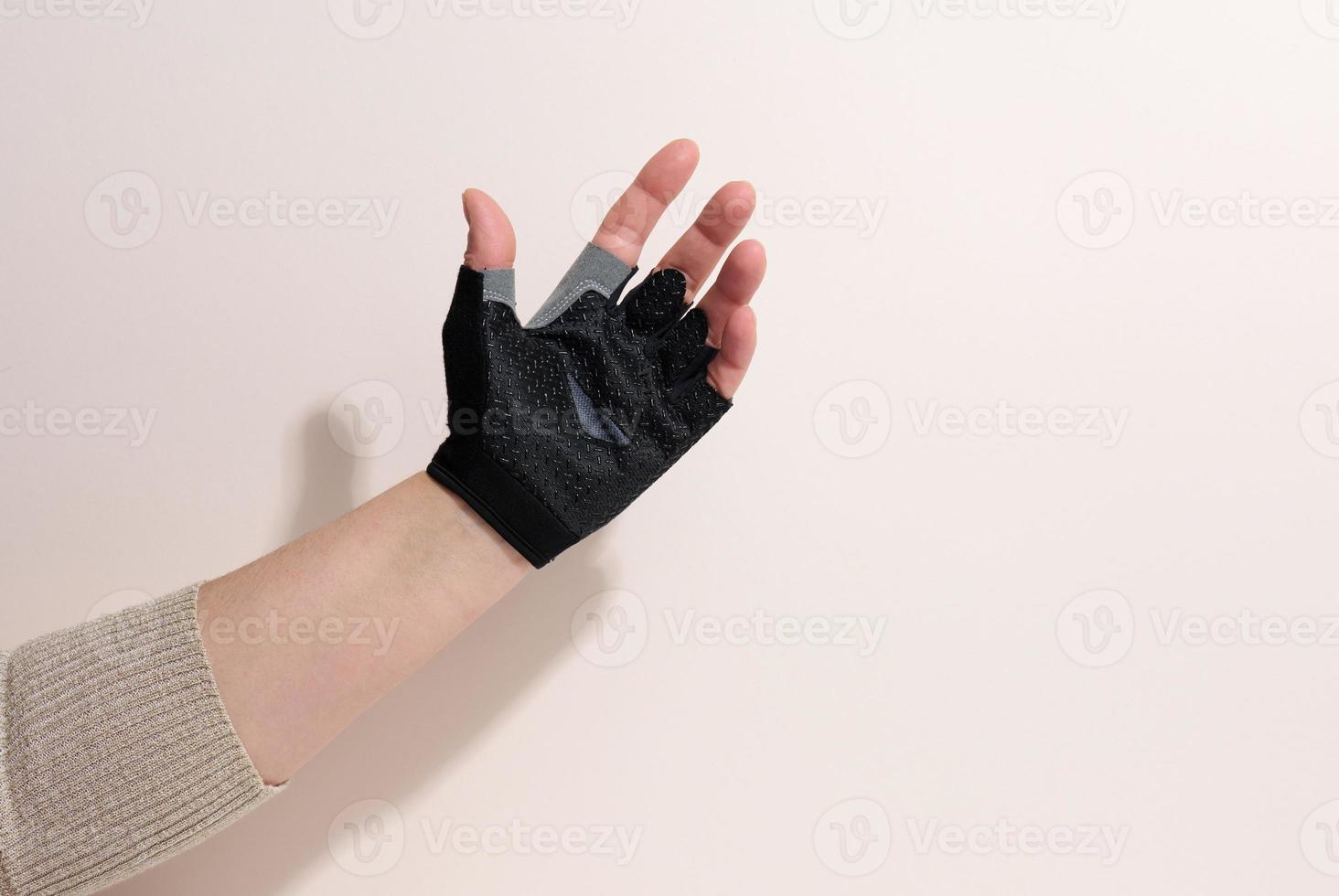zwart sport- handschoen Aan een vrouw hand, beige achtergrond. een deel van de lichaam is opgeheven omhoog foto