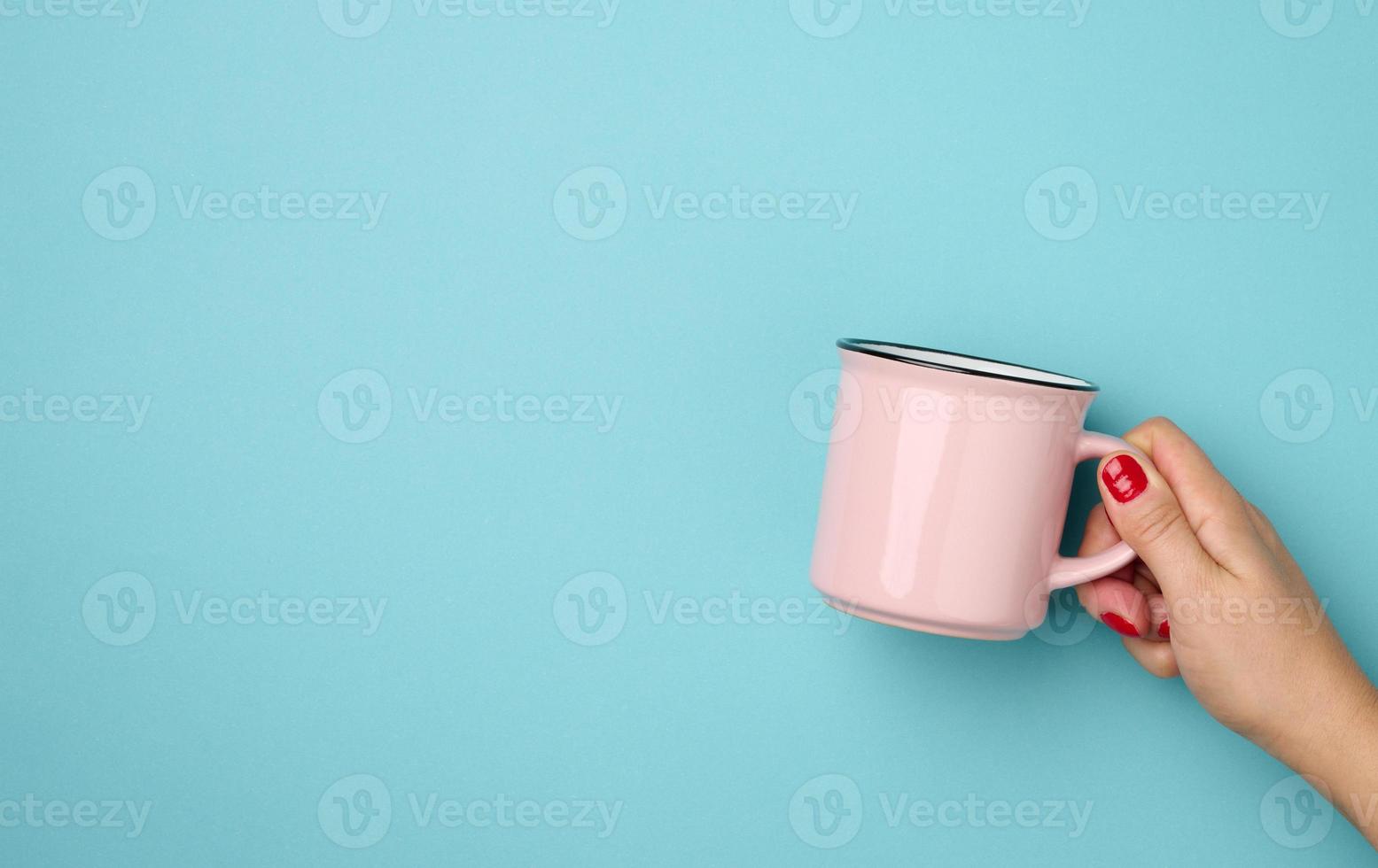 vrouw hand- Holding een roze keramisch mok Aan een blauw achtergrond, breken tijd en drinken koffie foto