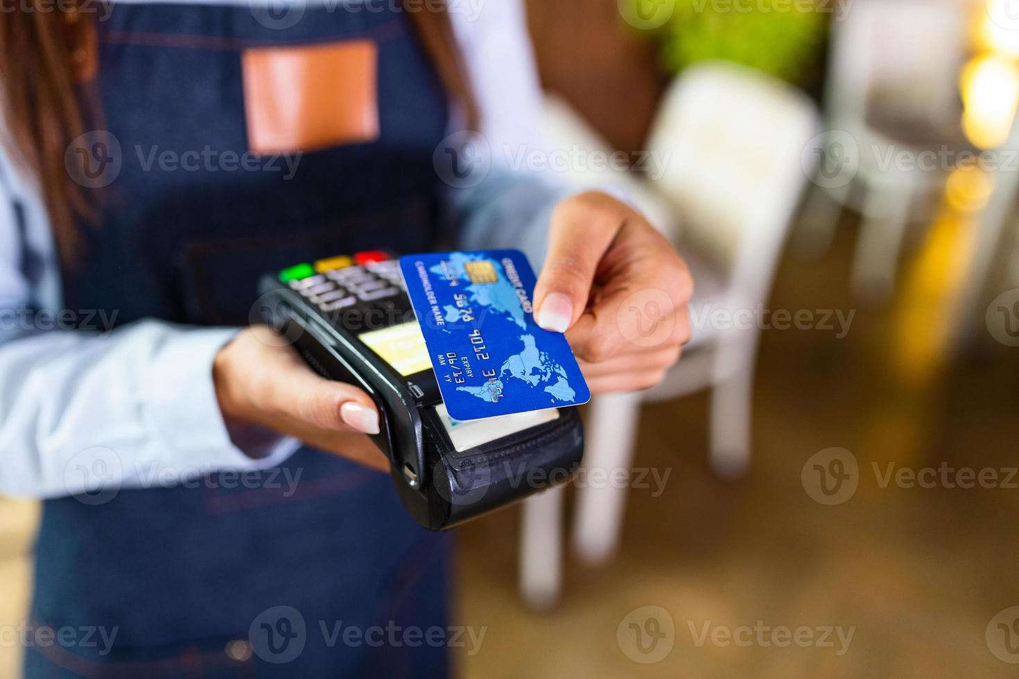 contactloos betaling concept, vrouw Holding credit kaart in de buurt nfc technologie Aan balie, cliënt maken transactie betalen Bill Aan terminal rfid Kassa machine in restaurant op te slaan, dichtbij omhoog visie foto