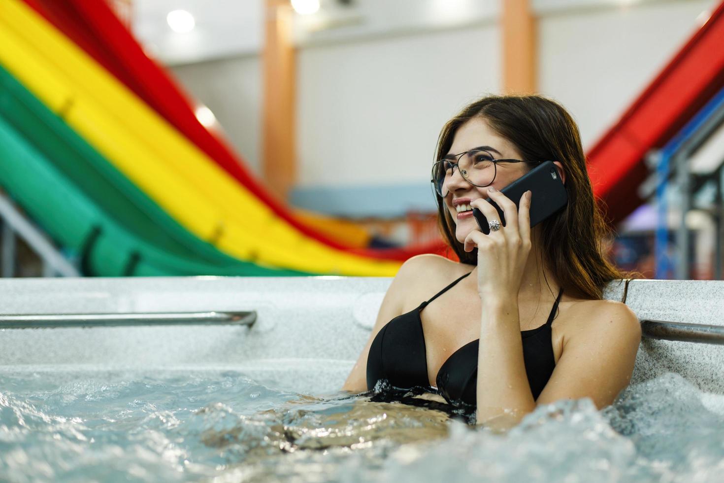 het mooie meisje, zittend in het zwembad en praten aan de telefoon foto