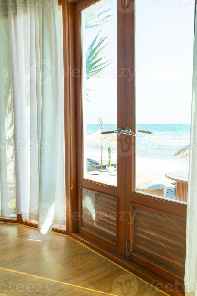 gordijn en glas venster met zee strand visie buiten foto