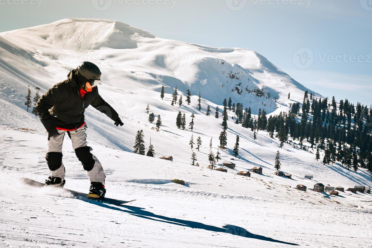 gelukkig snowboarder gekleed in donker zwart sportkleding rijden naar beneden de berg helling in Georgië, goderdzi Aan Kaukasus zonnig dag foto