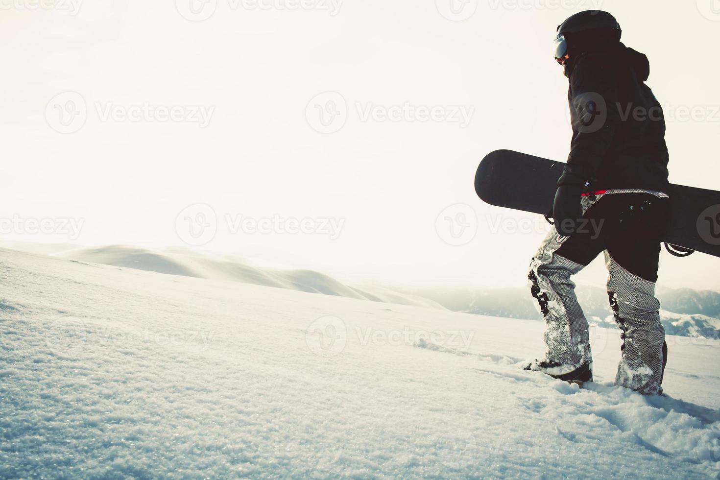 snowboarder gekleed in een vol beschermend uitrusting voor extreem gratis rit snowboarden poseren met een snowboard wandelen. geïsoleerd Aan grijs wit sneeuw achtergrond. foto