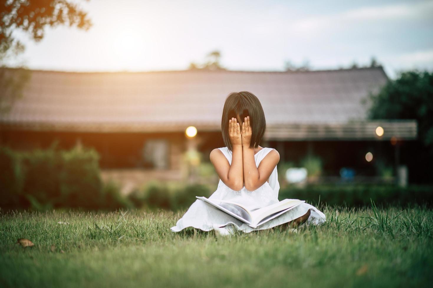 jong meisje lezen in de tuin buiten haar huis foto