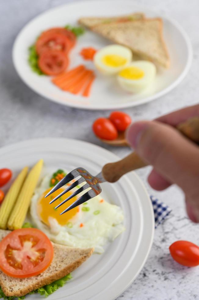 vork reiken naar gebakken eieren met brood met groenten als ontbijt foto