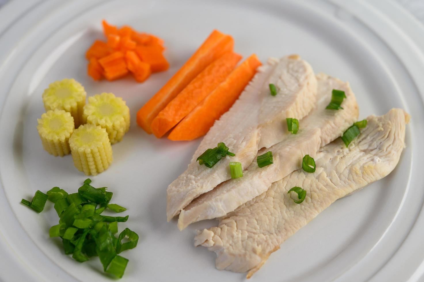 gestoomde kipfilet op een wit bord met lente-uitjes, babymaïs en worteltjes foto