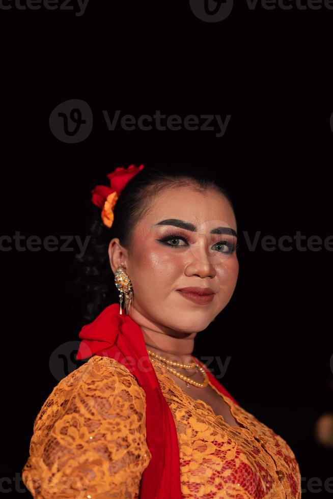 Javaans vrouw in een traditioneel oranje jurk terwijl vervelend bedenken en een rood sjaal Bij een dans festival foto