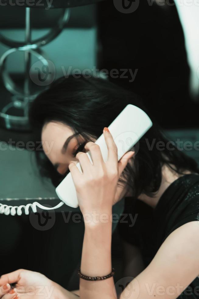 Aziatisch Dames maken een telefoon telefoontje terwijl vervelend een zwart jurk en armband in haar hand- foto