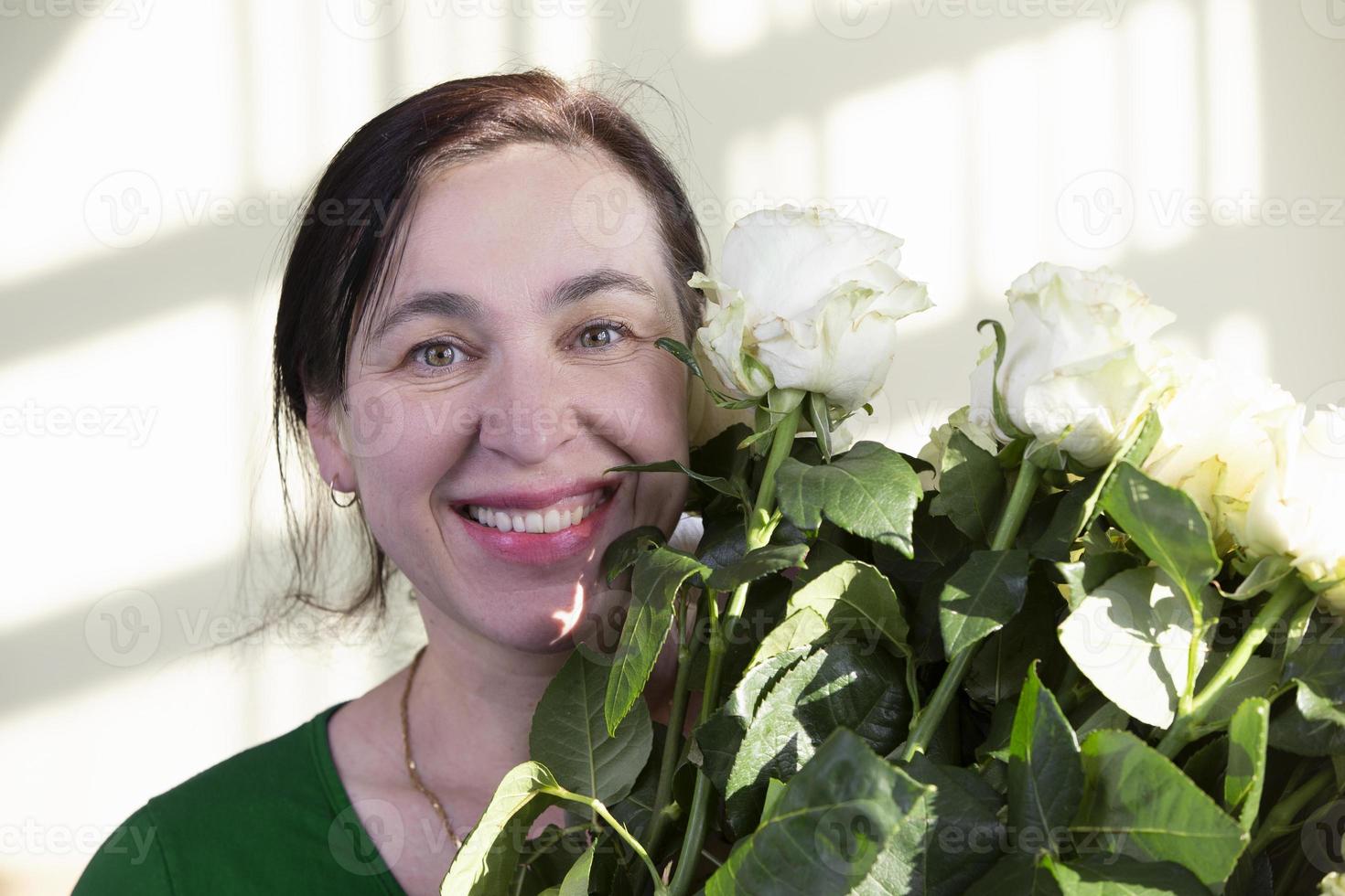 gelukkig midden- oud vrouw met boeket van rozen glimlachen en op zoek Bij camera.vrouw vijftig jaren oud. foto