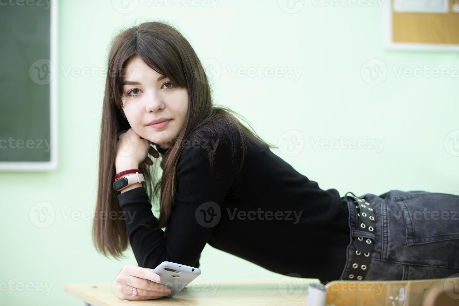 een tiener- meisje leugens Aan een school- bureau en looks in de camera. hoog school- leerling. foto