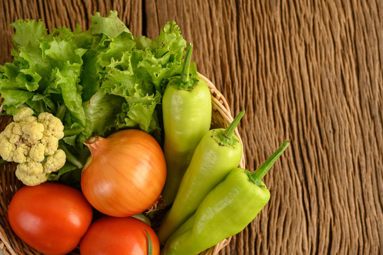 paprika, tomaat, ui, salade en bloemkool op een houten mand op een houten tafel foto