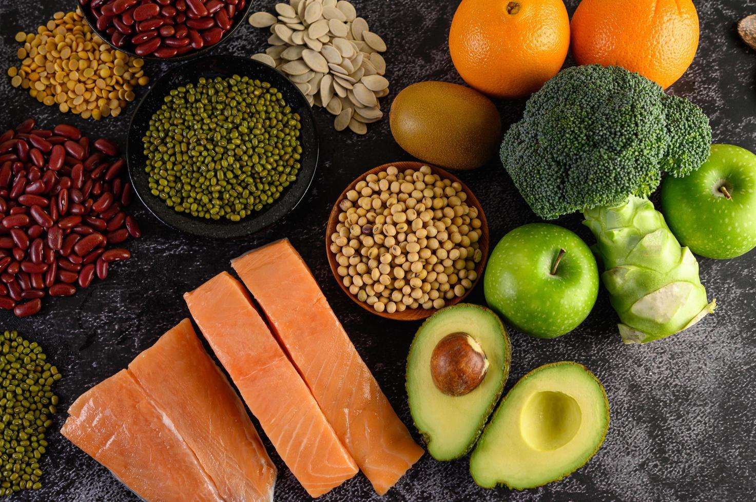 peulvruchten, broccoli, fruit en zalm op een zwarte cementachtergrond foto