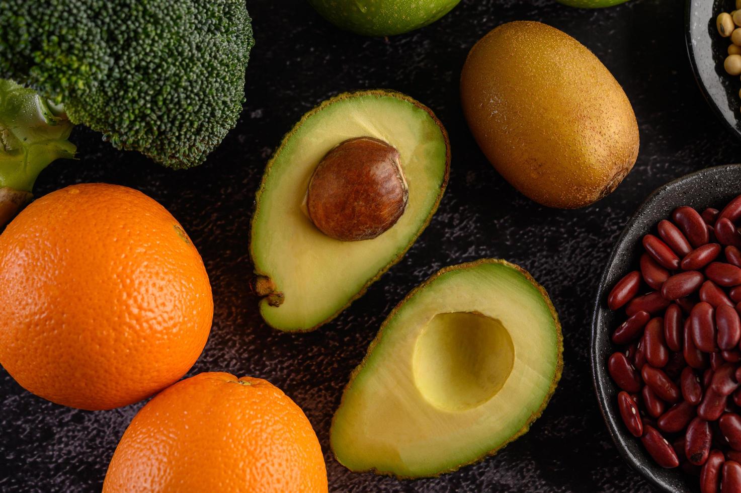 broccoli, appel, sinaasappel, kiwi, avocado en bonen op een zwarte cementvloer achtergrond foto