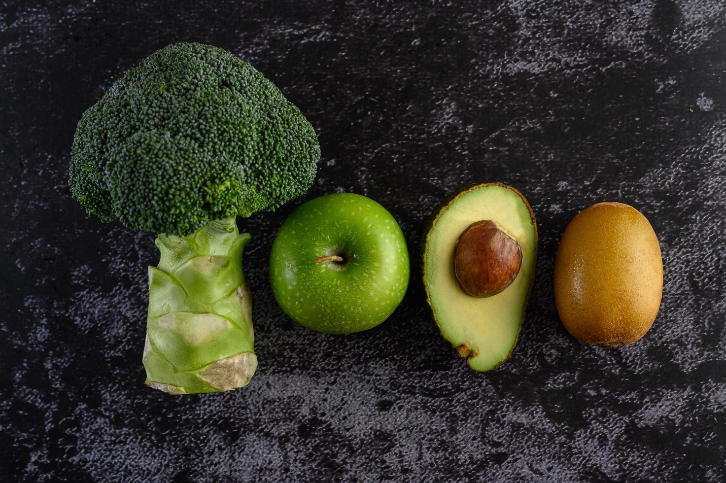 broccoli, appel, kiwi en avocado op de zwarte achtergrond van de cementvloer foto