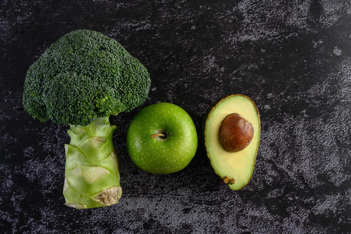 broccoli, appel en avocado op een zwarte cementvloer achtergrond foto