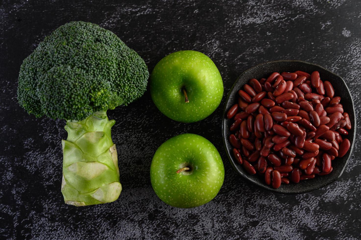 broccoli, appel en bonen op een zwarte cementvloer achtergrond foto