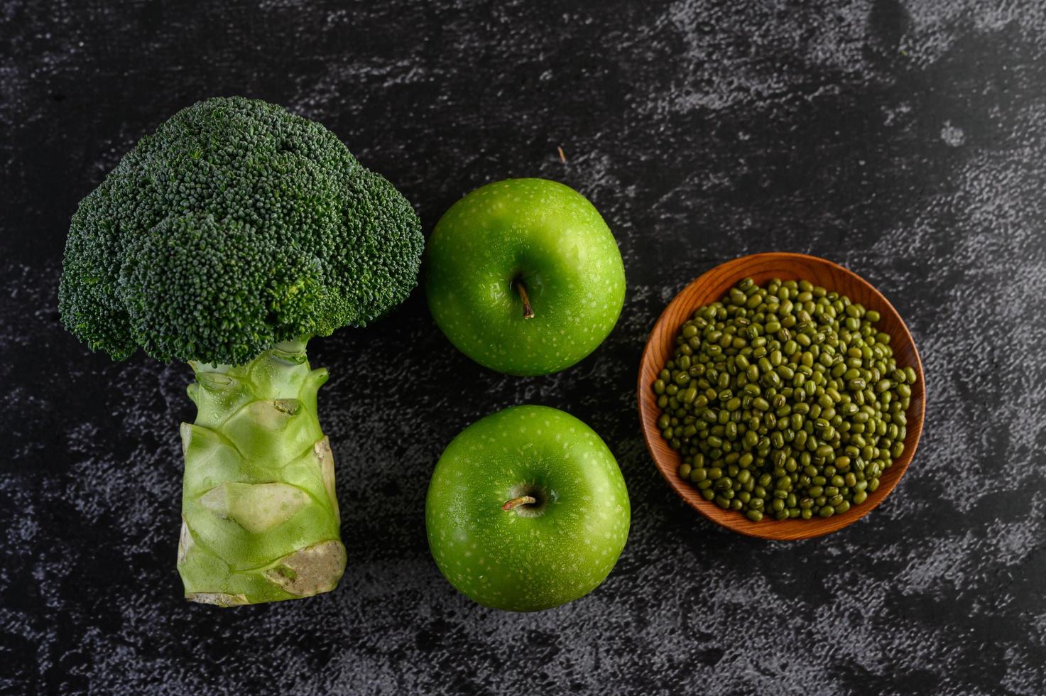 broccoli, appel en groene bonen op een zwarte cementvloer achtergrond foto
