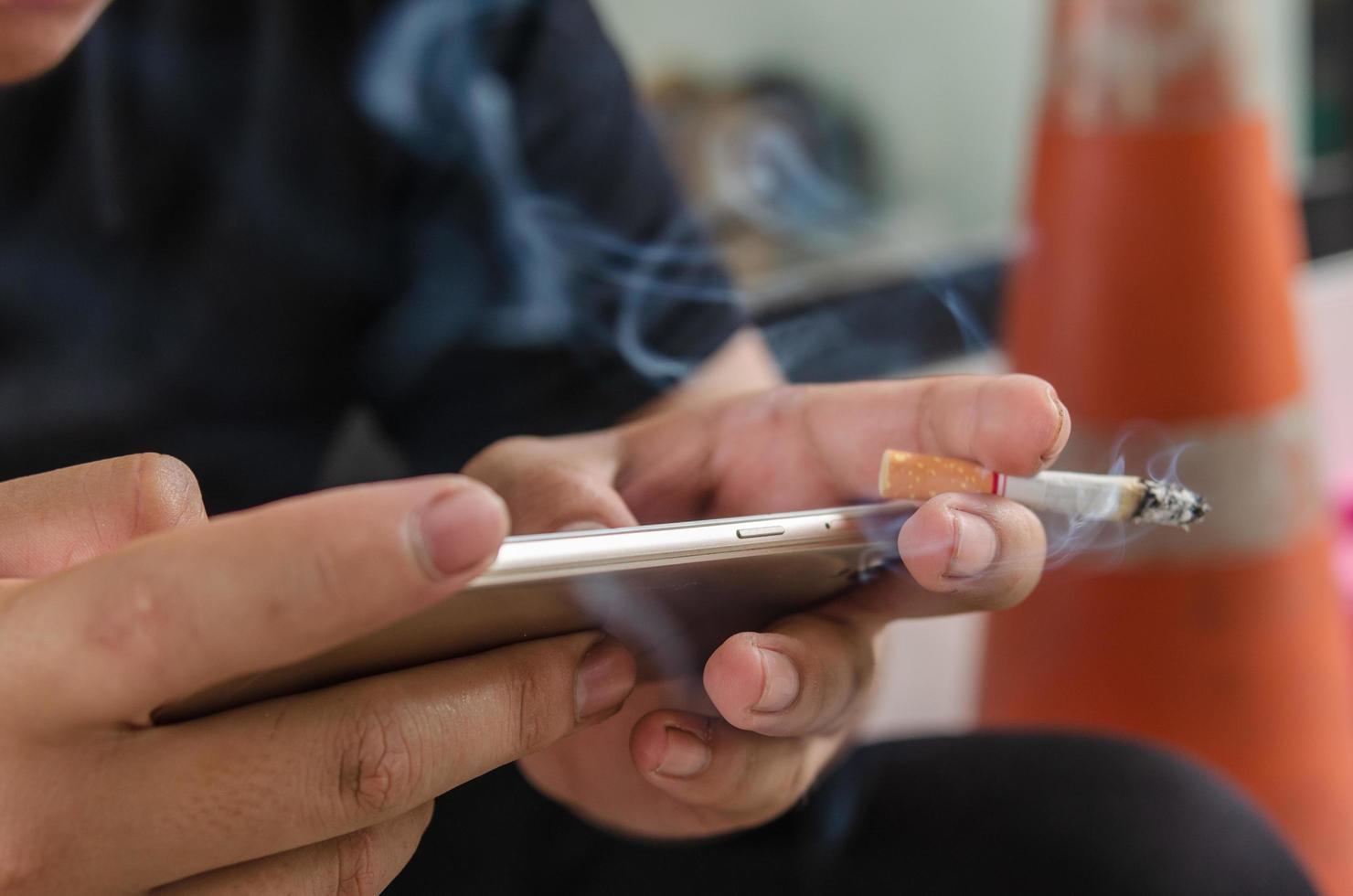 persoon die een sigaret rookt tijdens het sms'en op een slimme telefoon foto