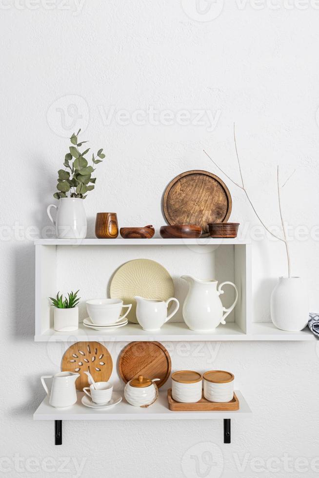 een reeks van wit elegant Open schappen met divers keramisch wit borden, milieuvriendelijk houten borden. wit getextureerde muur. keuken zonder afval. foto