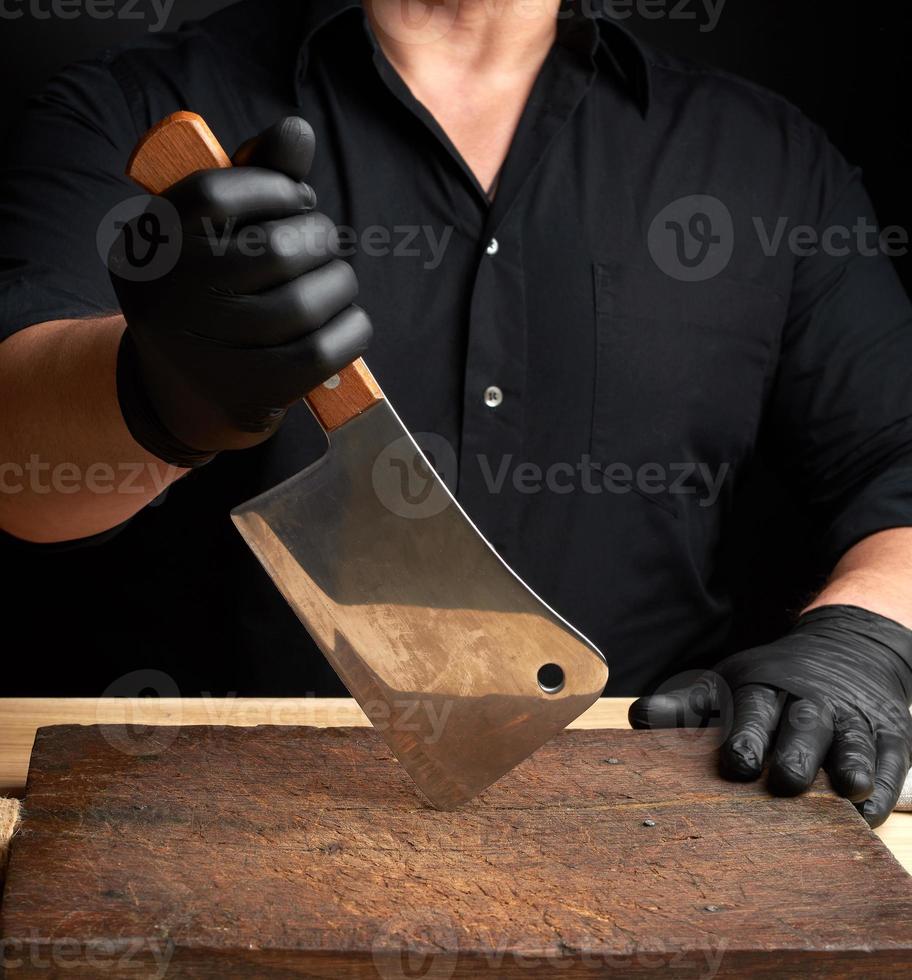 chef in een zwart overhemd en zwart latex handschoenen houdt een groot keuken mes foto