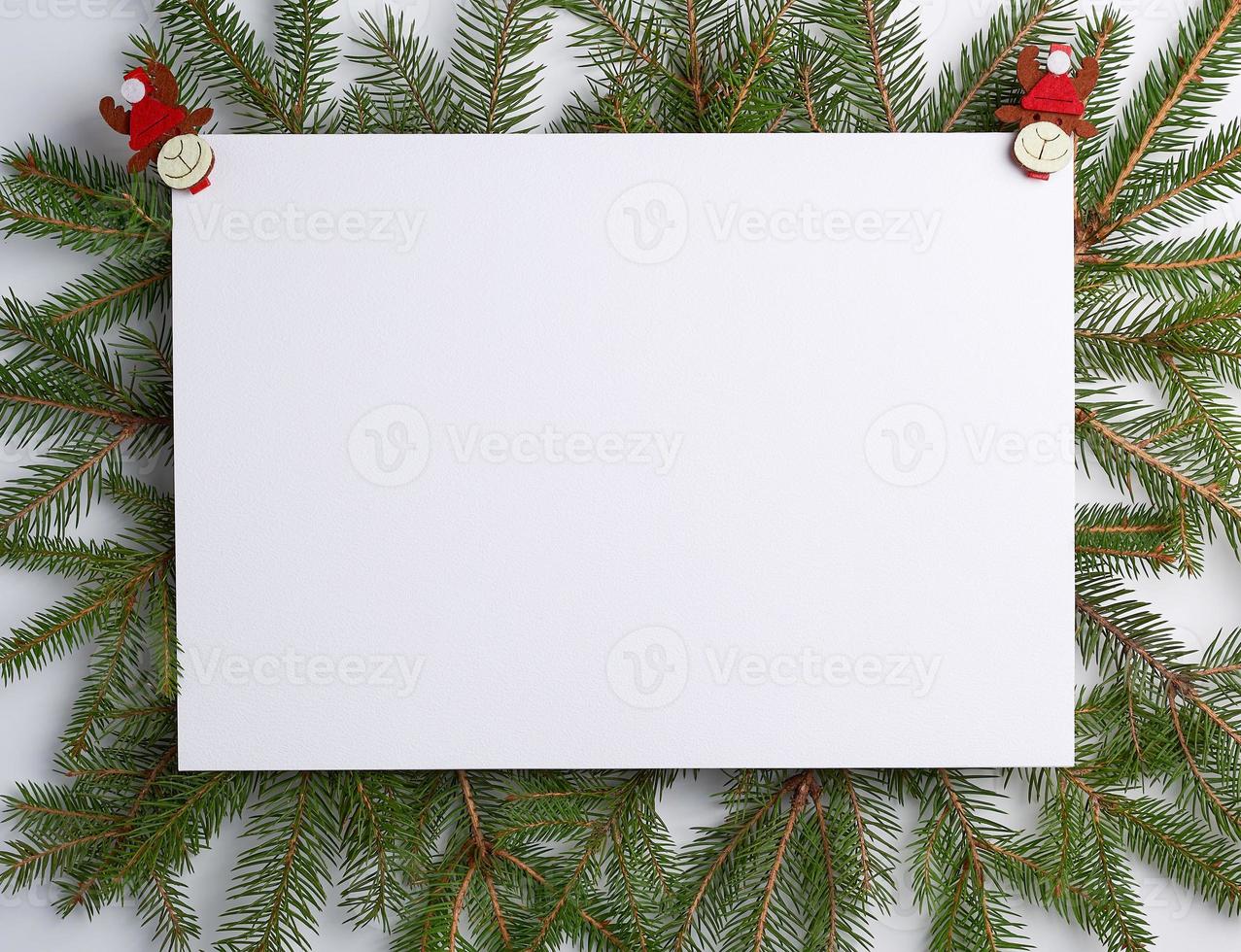 felicitatie- Kerstmis achtergrond met een leeg wit vel en groen takken van net versierd met vakantie speelgoed foto