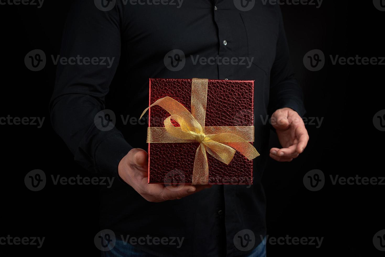 volwassen Mens in een zwart overhemd houdt een rood plein doos met een geknoopt boog foto