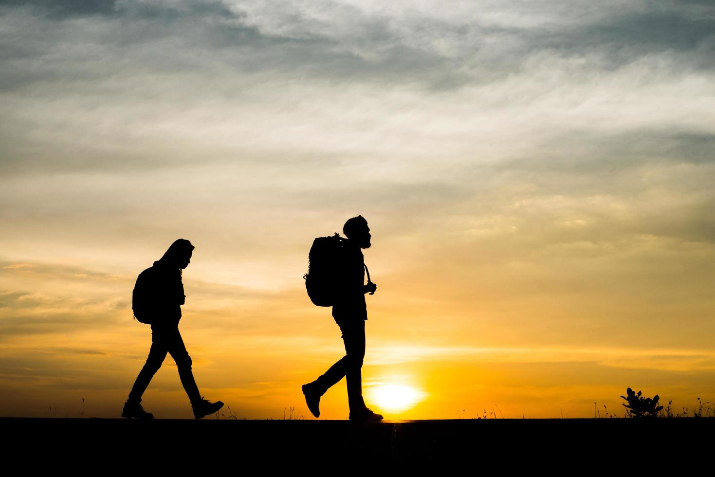 silhouetten van twee wandelaars met rugzakken die van de zonsondergang genieten foto