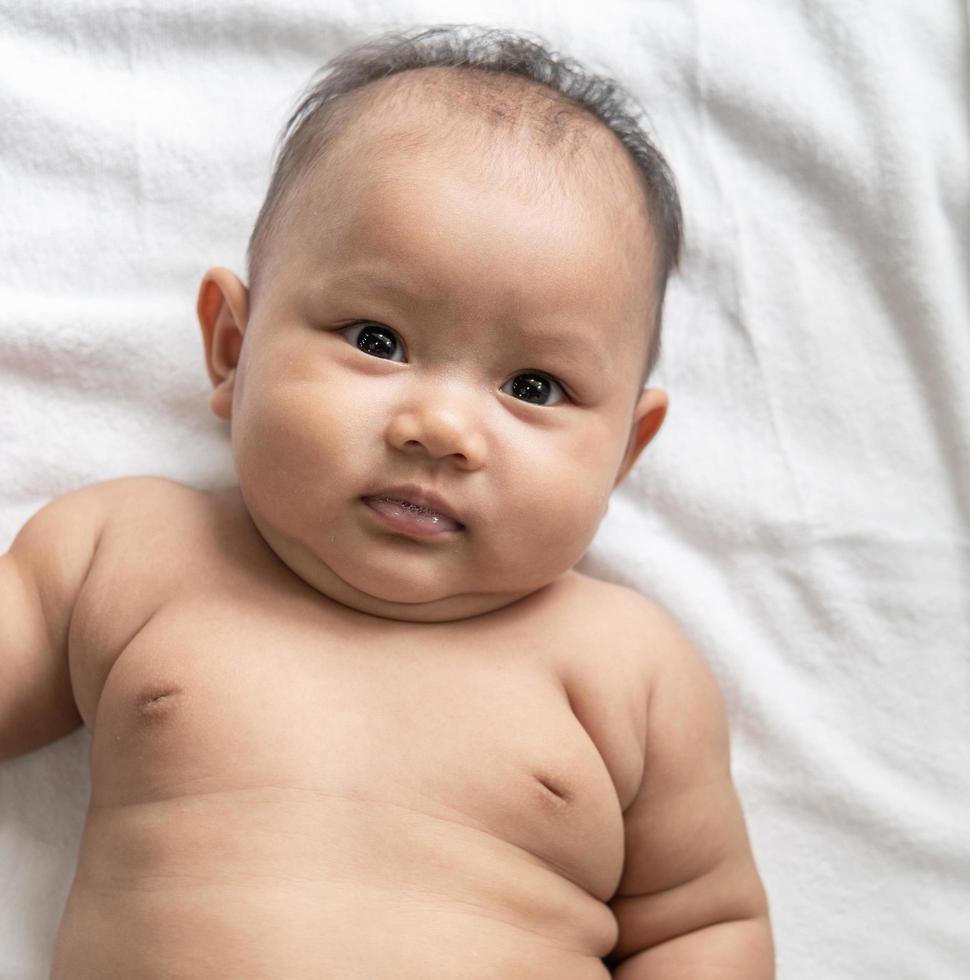 baby liggend met zijn gezicht omhoog op een wit bed en kijkt naar de camera foto