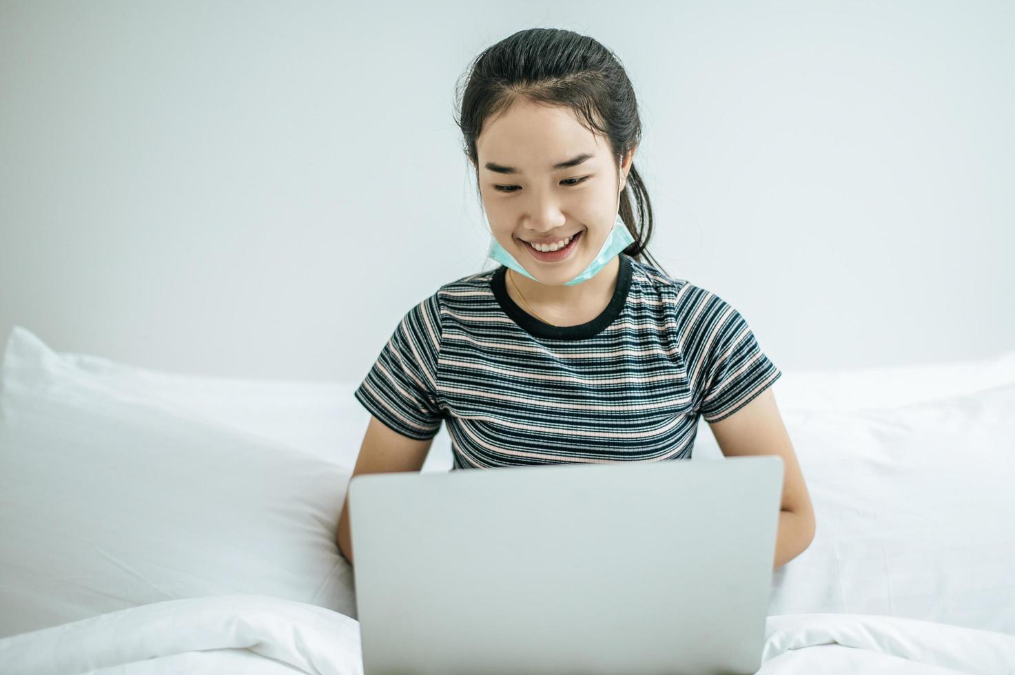 een jonge vrouw die op haar laptop in bed speelt foto