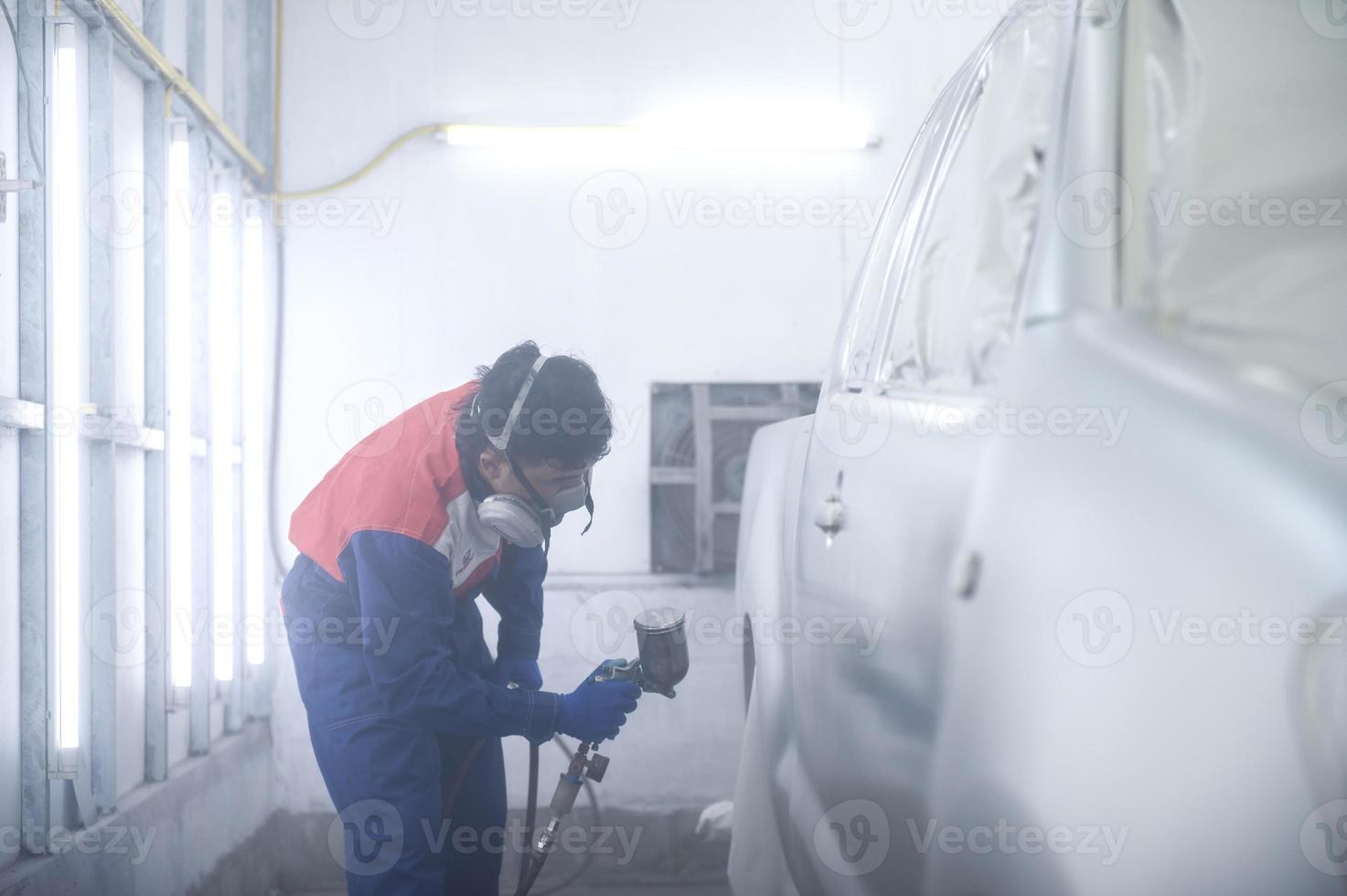 Aziatisch auto monteur vervelend beschermend pak en gasmasker verven auto lichaam bumpers in verf kamer, spuiten auto's in verf kamer foto