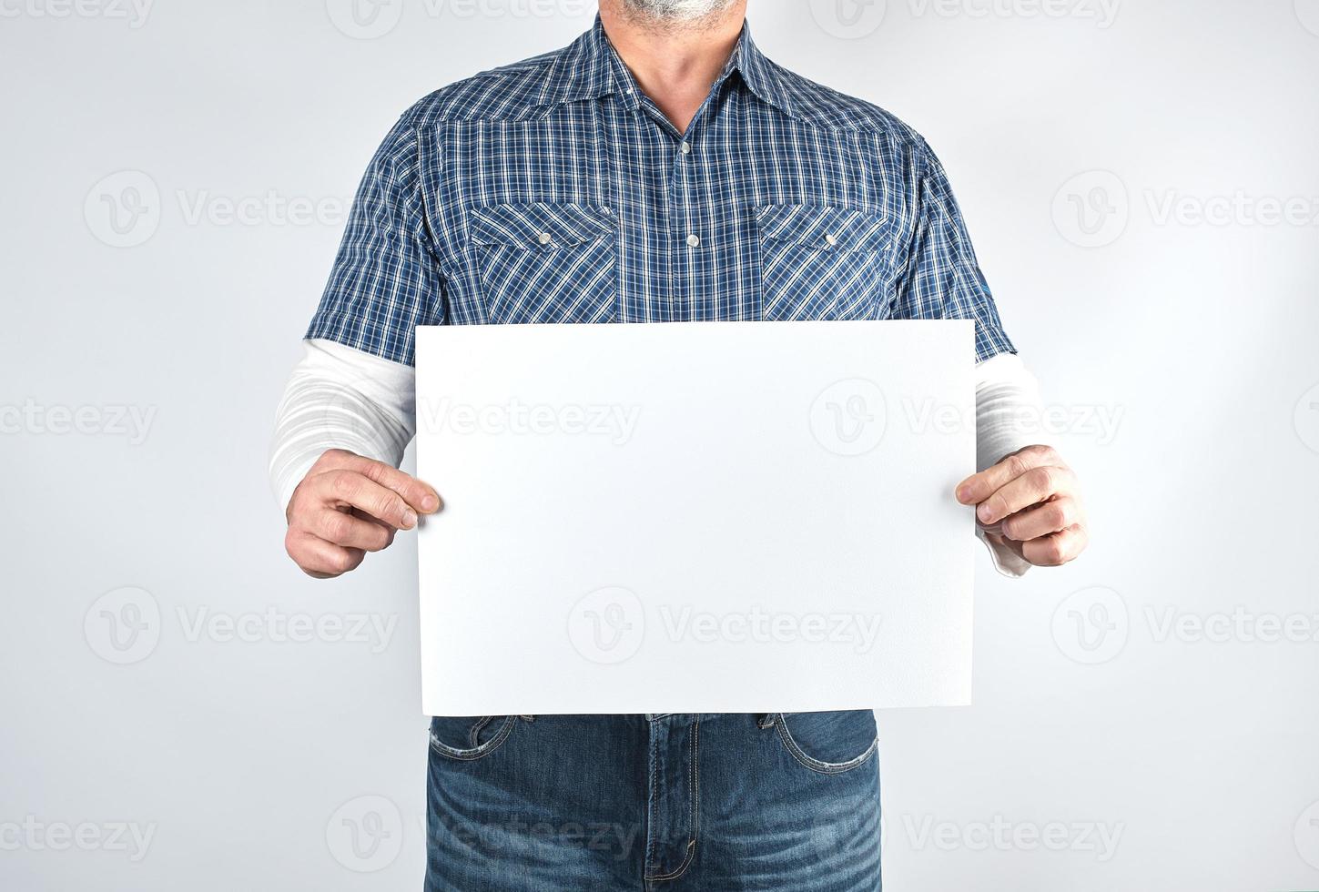 Mens in een blauw plaid overhemd en jeans is Holding een blanco rechthoekig wit papier vel foto