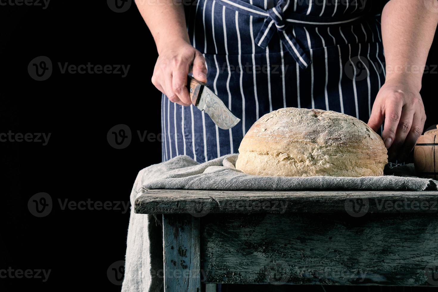 vrouw in een schort met een mes in haar hand- over naar besnoeiing ronde gebakken brood foto