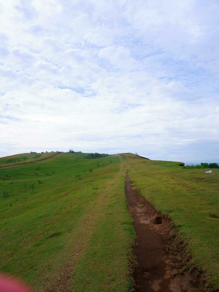 groen gras veld- Aan klein heuvels en blauw lucht met wolken en aarde trails in Indonesië foto