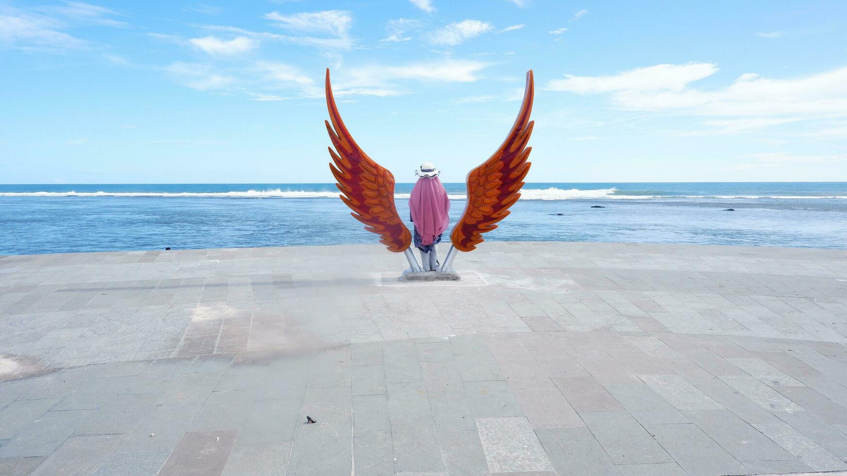 vrouw staand in de midden- van een vleugel standbeeld Aan de strand foto