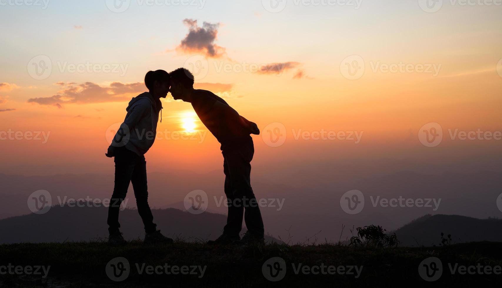 silhouet van een paar Aan de berg, een jong romantisch paar genieten een mooi visie van de zon instelling over- de bergen, liefde, Valentijnsdag dag. foto