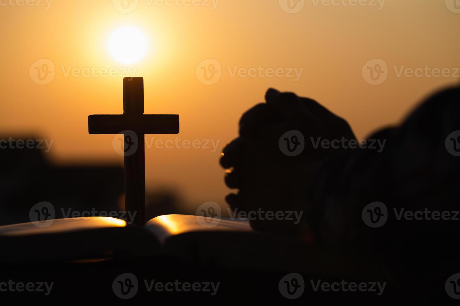 silhouet van christelijke jonge vrouw bidden met een kruis en open de Bijbel bij zonsopgang, christelijke religie concept achtergrond. foto