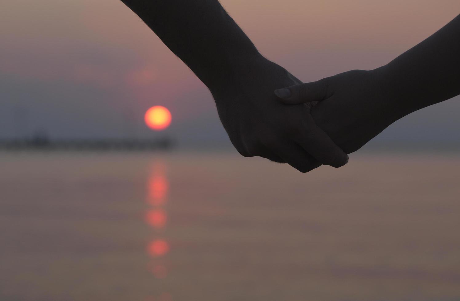 paar hand in hand bij zonsondergang foto