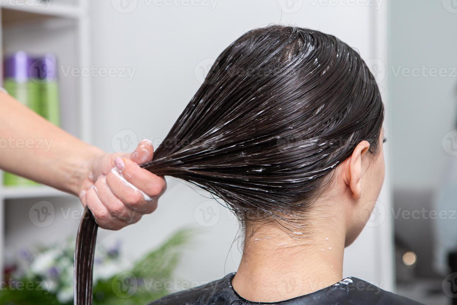 kapper is van toepassing een haar- masker naar Rechtdoor zwart haar. haar- zorg Bij de schoonheid salon. foto