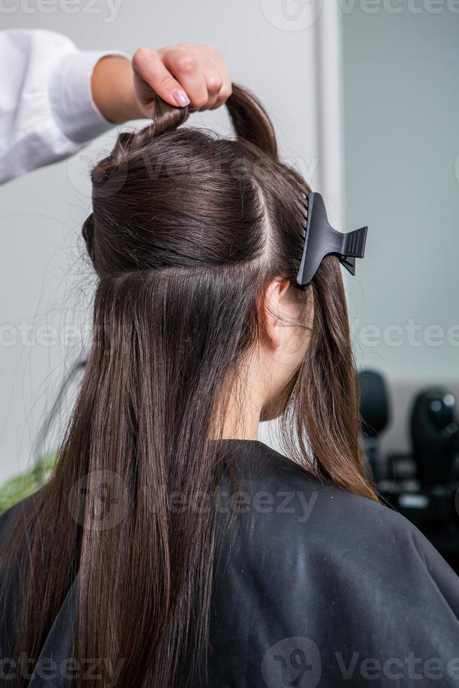 kapper is van toepassing een haar- masker naar Rechtdoor zwart haar. haar- zorg Bij de schoonheid salon. foto