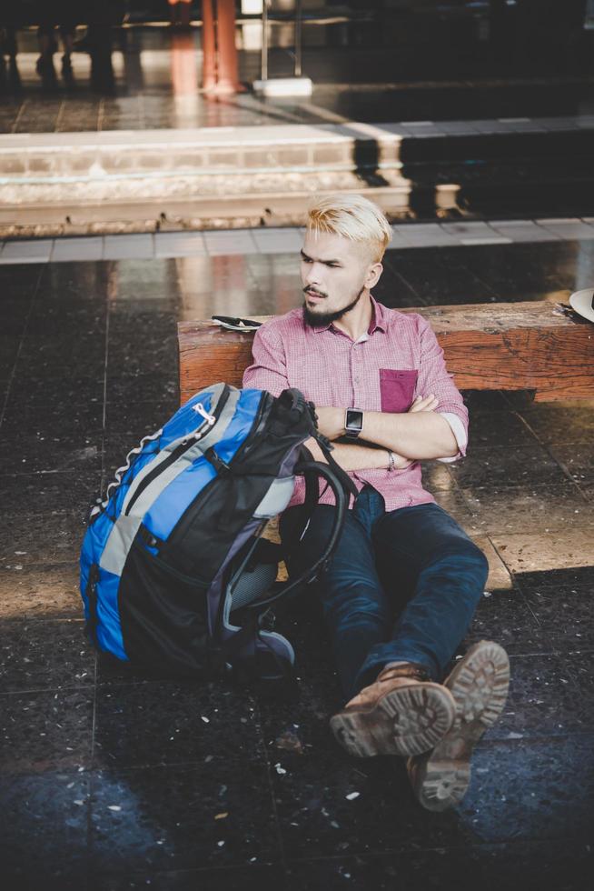 jonge hipster man zittend op een houten bankje op het treinstation foto