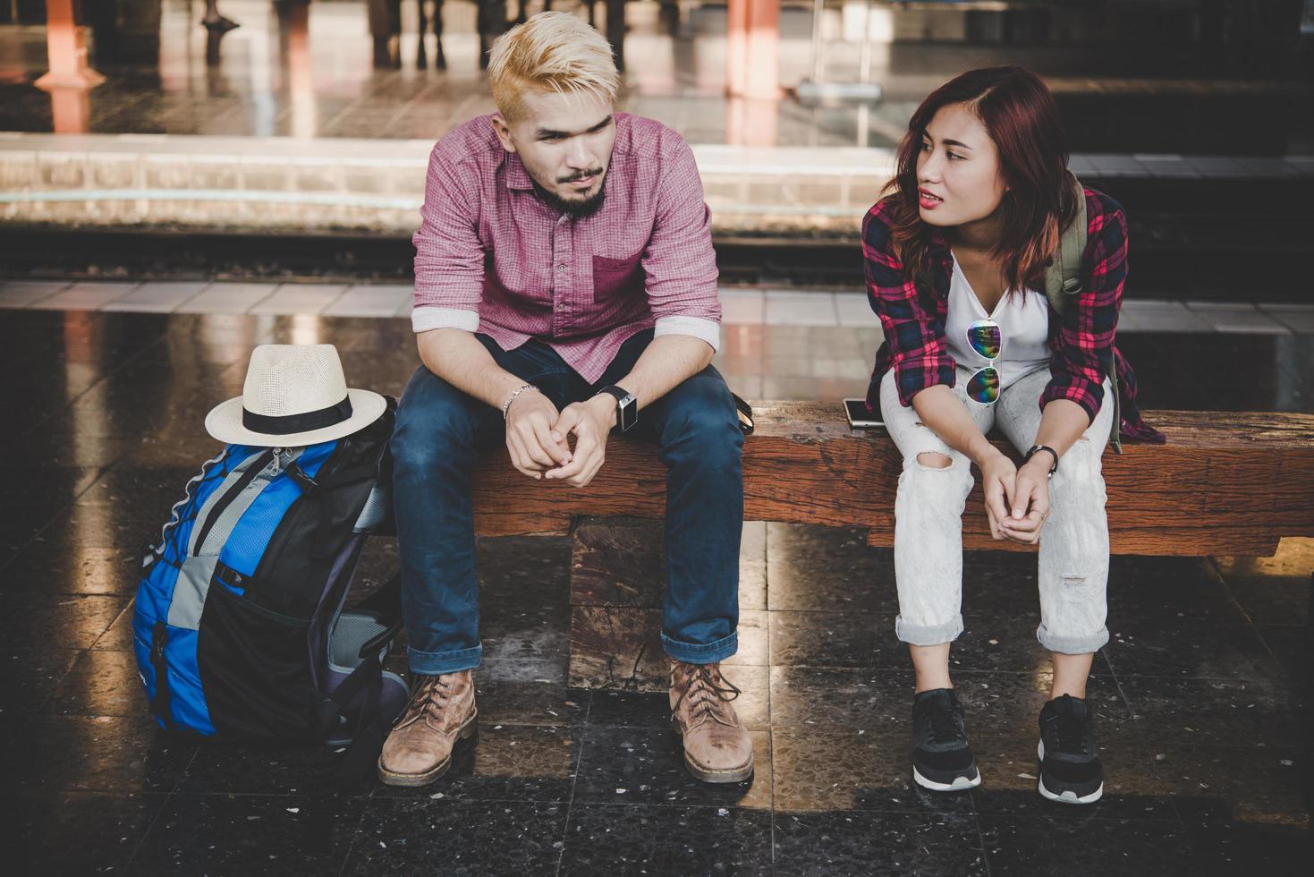 jonge hipster paar zittend op een houten bankje op het treinstation foto