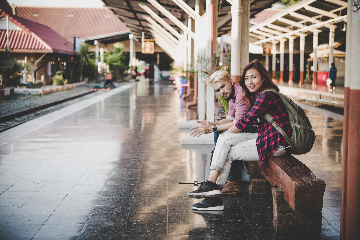 jonge hipster paar zittend op een houten bankje op het treinstation foto