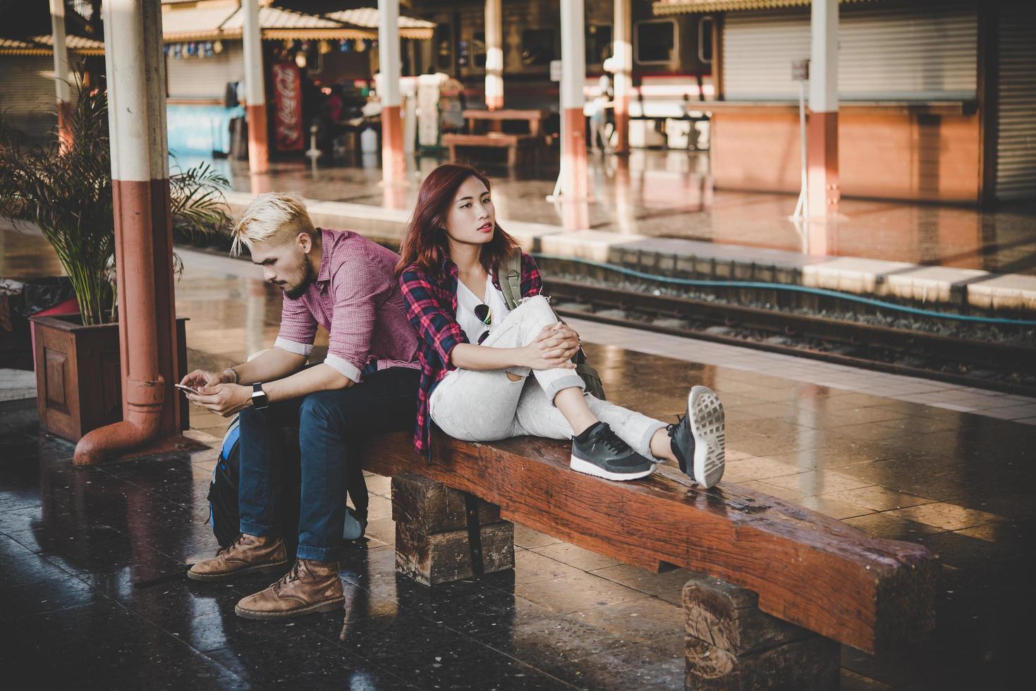jonge hipster paar zittend op een houten bankje op het treinstation foto